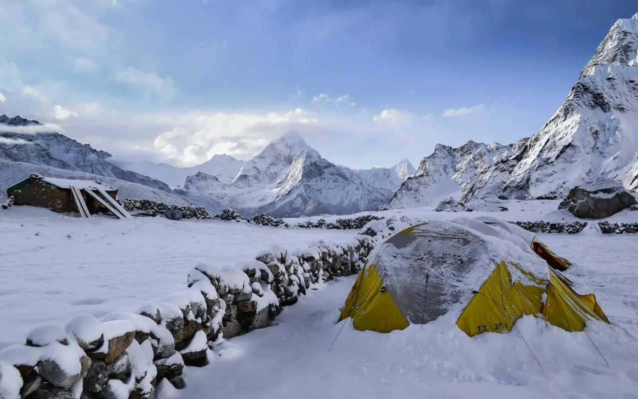 Yellow tents in deep snow below snowy peaks