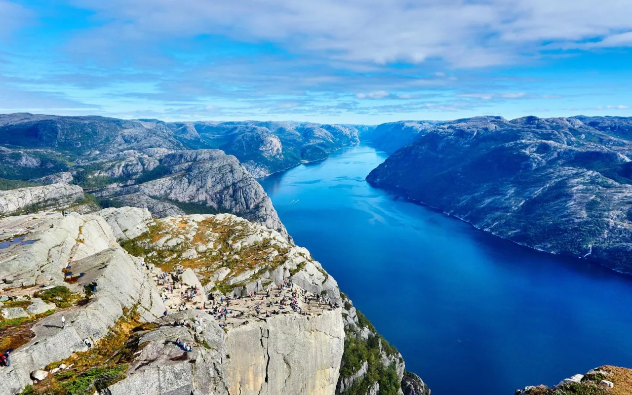 A steep cliff above a deep blue fjord under a clear sky