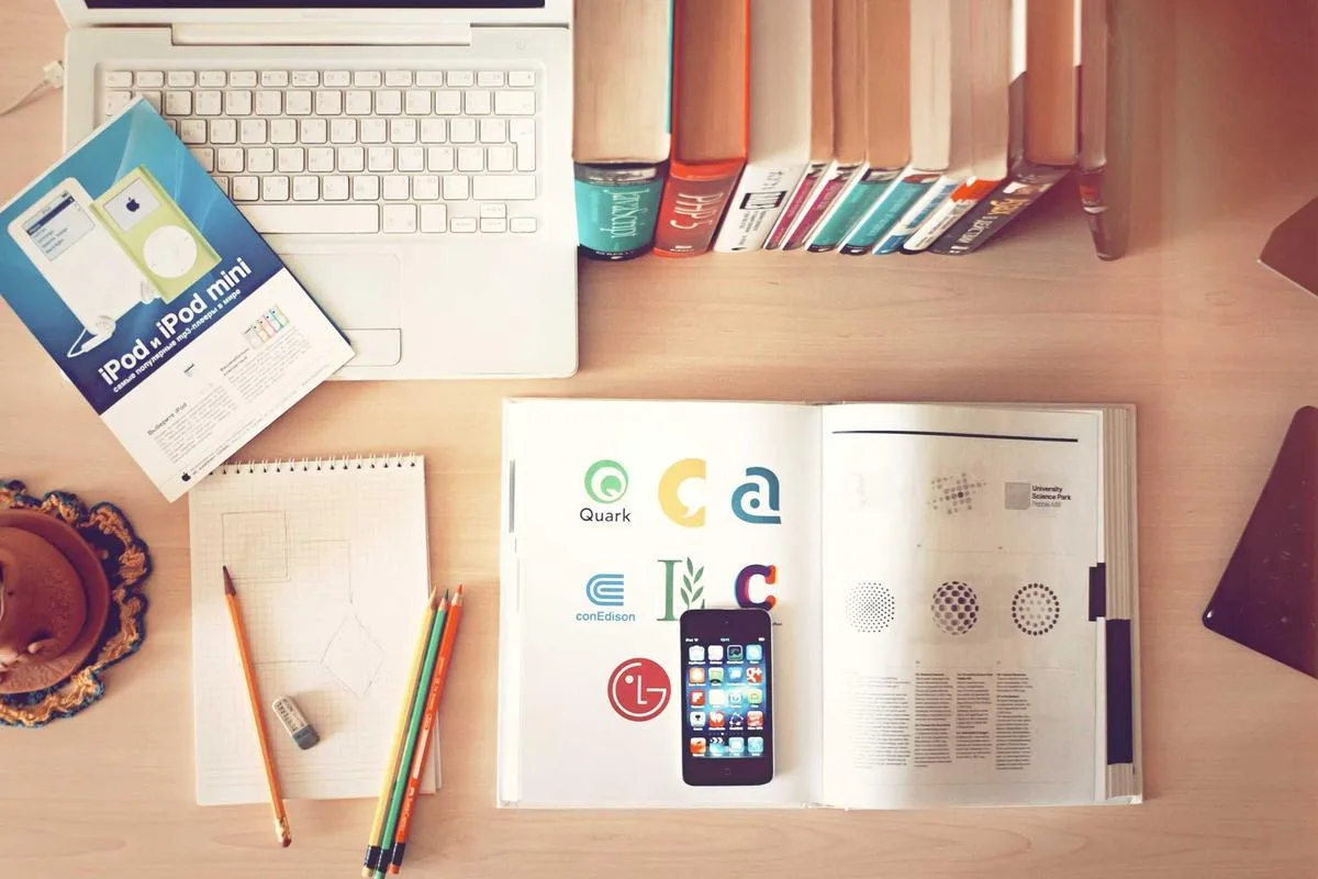 Top-down view of a desk with a laptop, sketches, a phone and books